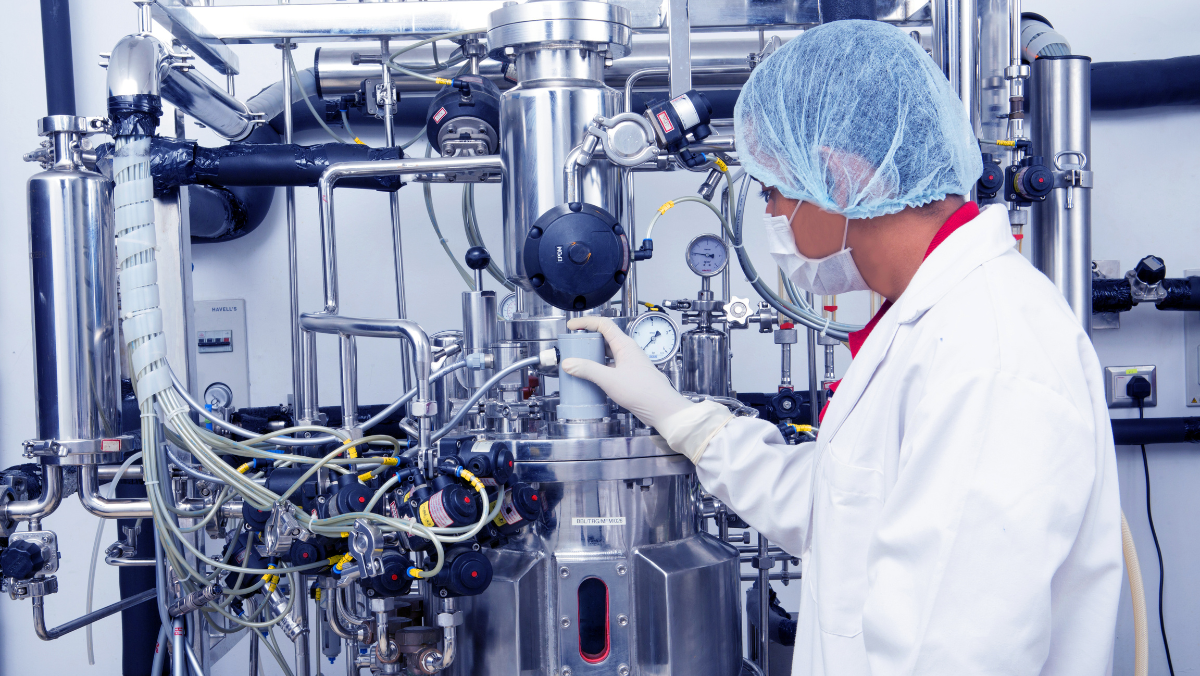 Biomanufacturing technician monitoring large-scale pharmaceutical fermentation equipment